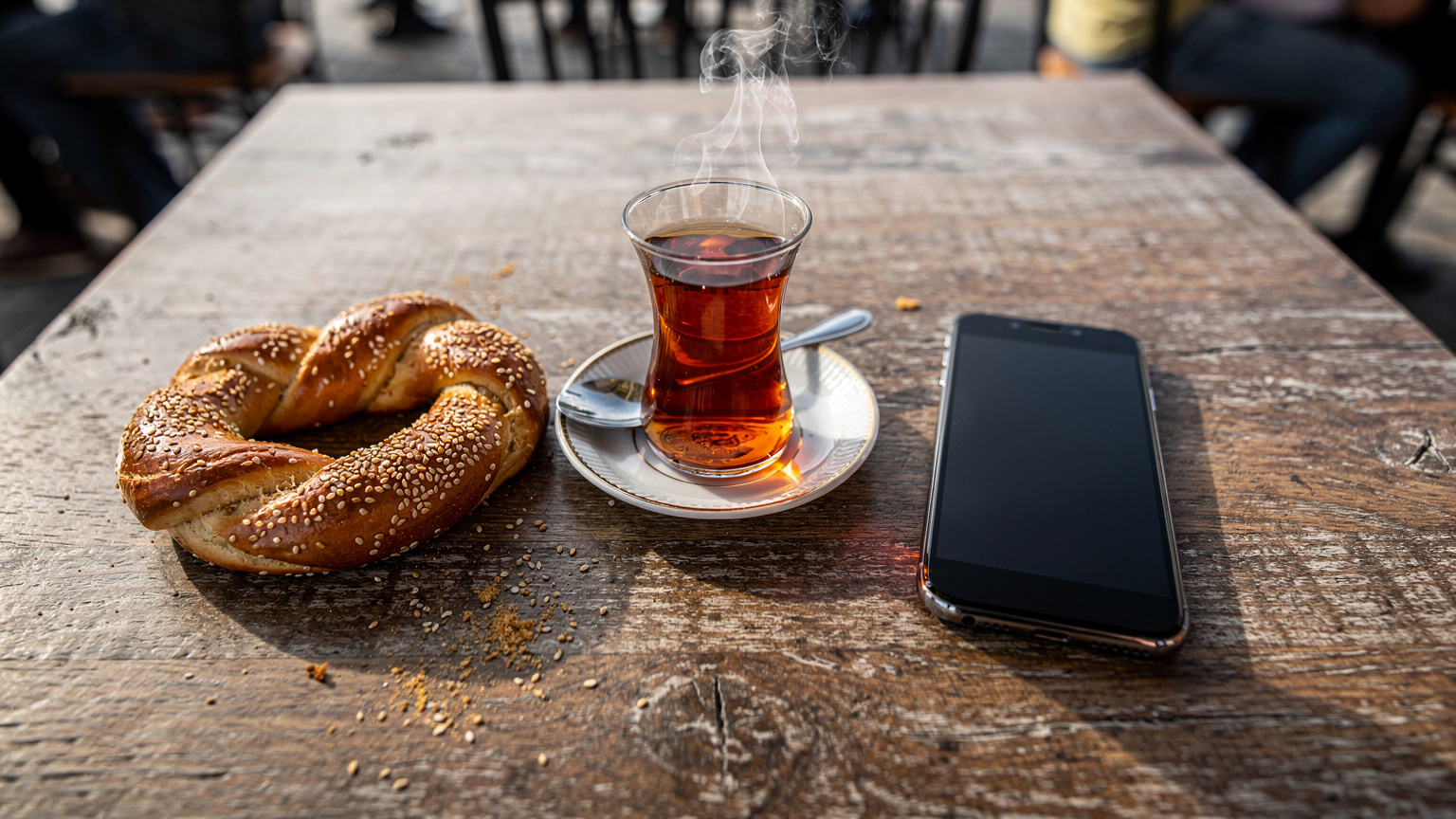 İstanbul'un Karaköy semtindeki bir çay bahçesinde, masada duran geleneksel ince belli çay bardağı, simit ve akıllı telefonun yakından çekilmiş bir fotoğrafı.