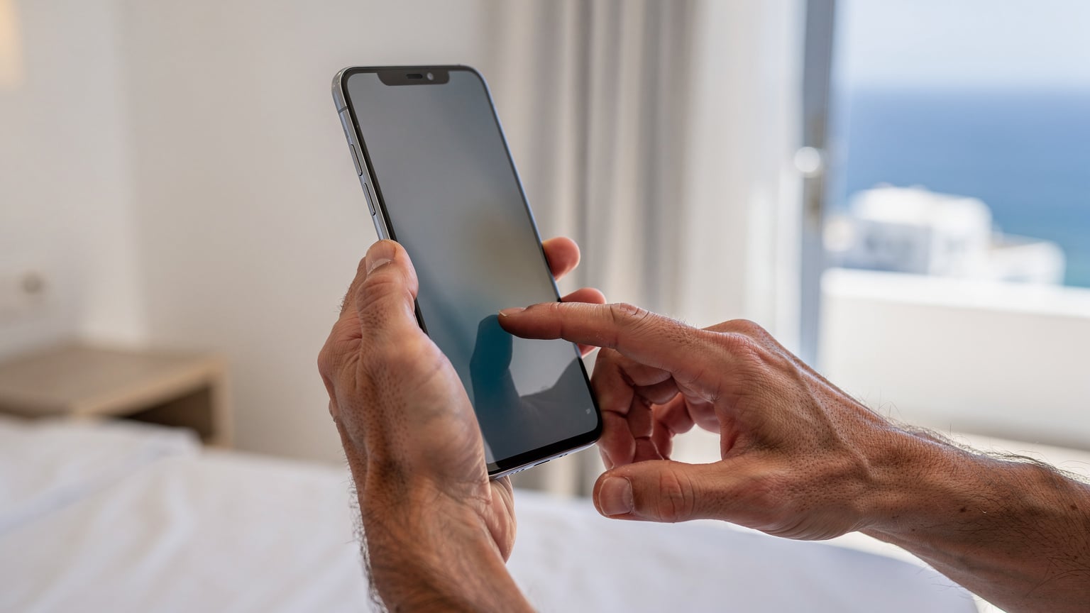 Close-up of hands holding a smartphone in a sunlit hotel room in Mykonos, with a finger gently tapping the screen to confirm an eSIM installation.