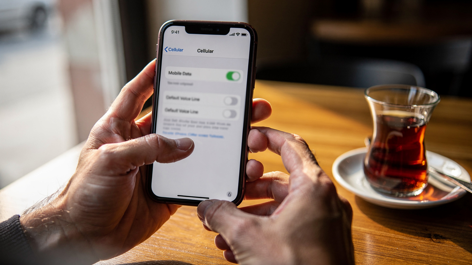 Eine Nahaufnahme von Händen, die ein iPhone 11 halten, während auf dem Bildschirm die Dual-SIM-Optionen für die Datennutzung und Anrufeinstellungen angezeigt werden.