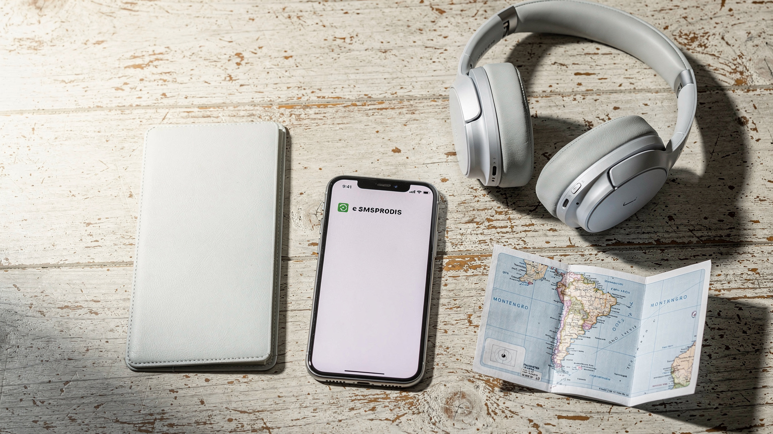 Ein Overhead-Flat-Lay zeigt einen geöffneten Reisepass, ein Smartphone mit eSIM-Profil, Kopfhörer und eine Karte von Montenegro, alles auf einem Holztisch mit natürlichem Licht.