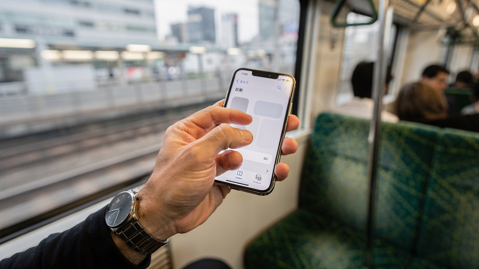 Nahaufnahme einer Hand, die ein Smartphone hält, auf dem ein eSIM-Profil im Menü zur Netzauswahl eines Zuges der JR East auf der Yamanote-Linie in Tokio aktiviert wird.