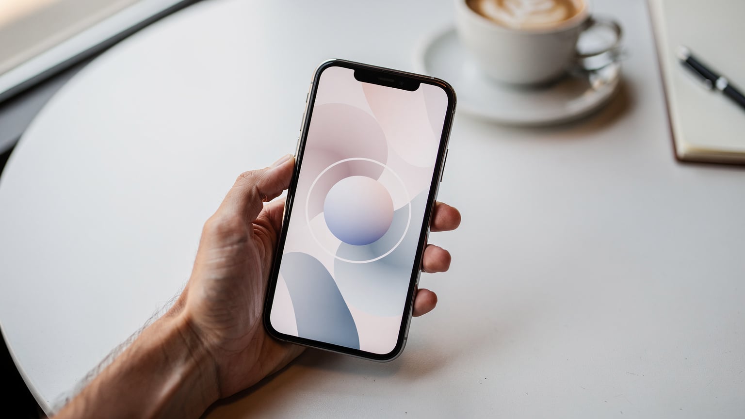 Paparan skrin telefon pintar menunjukkan aplikasi MyDigi yang sedang memuatkan maklumat akaun, dengan tangan memegang telefon di atas meja kafe yang ringkas.