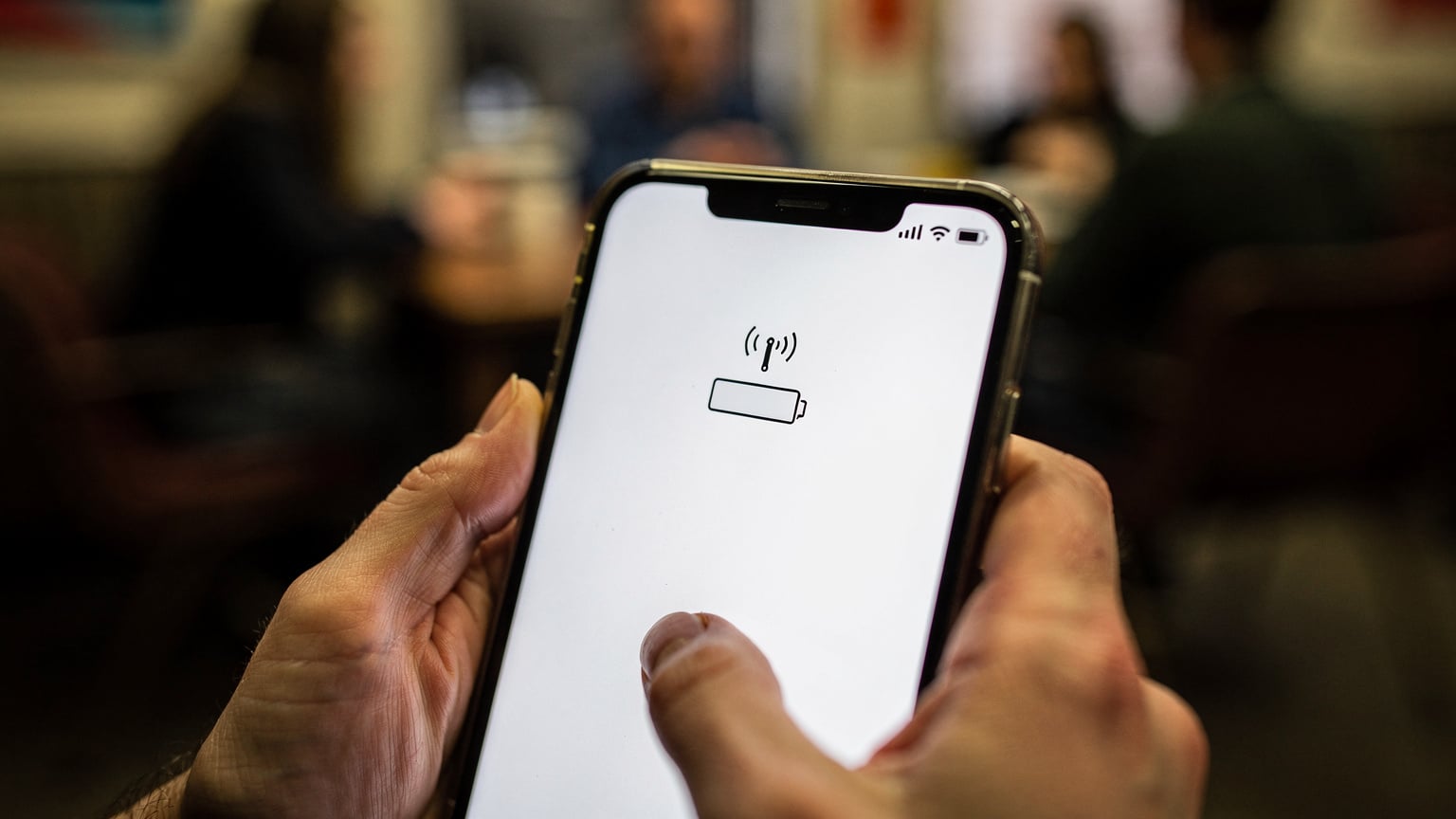 A close-up shot of a traveler's hands holding a smartphone, zoomed in on the battery and signal icons, indicating a low data speed or limited signal strength.