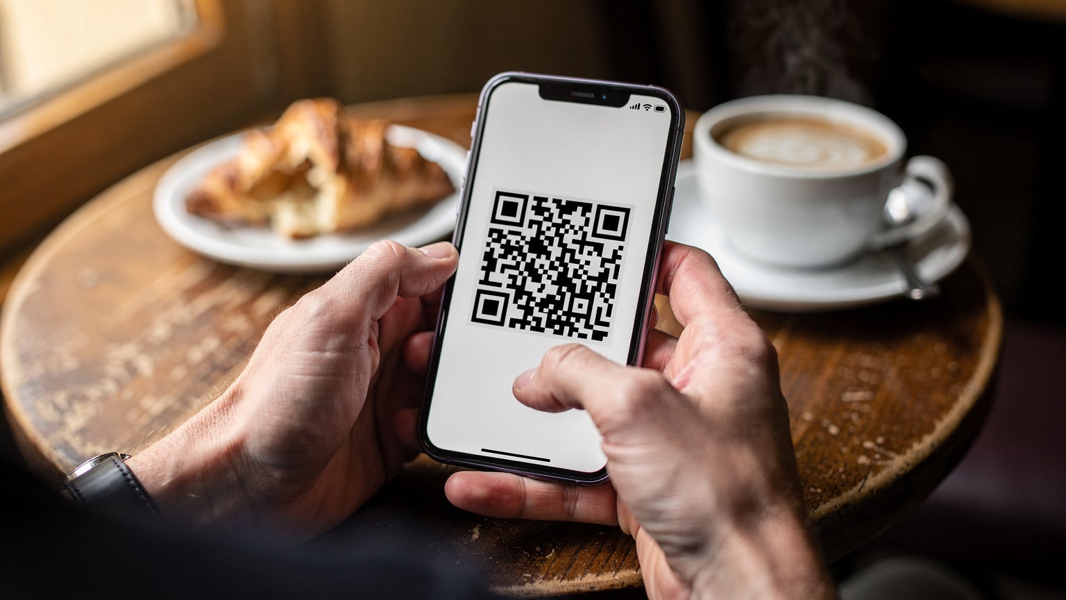 A close-up shot of a traveler's hands in a French cafe, holding a smartphone, actively scanning a QR code for eSIM activation, with a croissant and coffee on the table, emphasizing the ease of setup before travel.