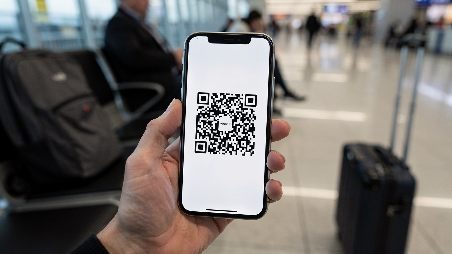 Une main tenant un smartphone affichant un QR code d'activation d'eSIM, avec en arrière-plan flou, des bagages et une salle d'attente d'aéroport bondée, suggérant un départ imminent.