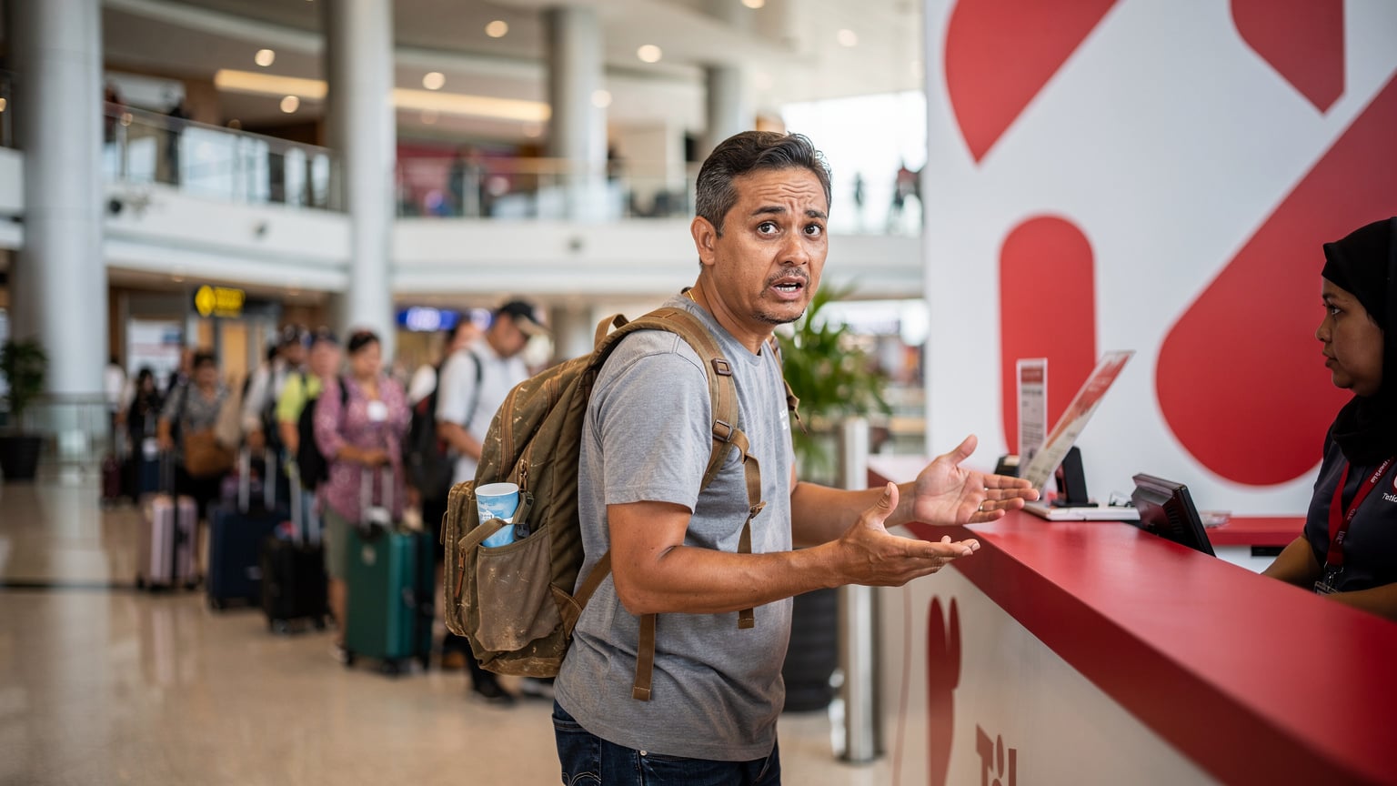 A traveler looking slightly frustrated at a busy Telkomsel counter inside Ngurah Rai International Airport, Bali, trying to register a new SIM card amidst a line of other tourists.