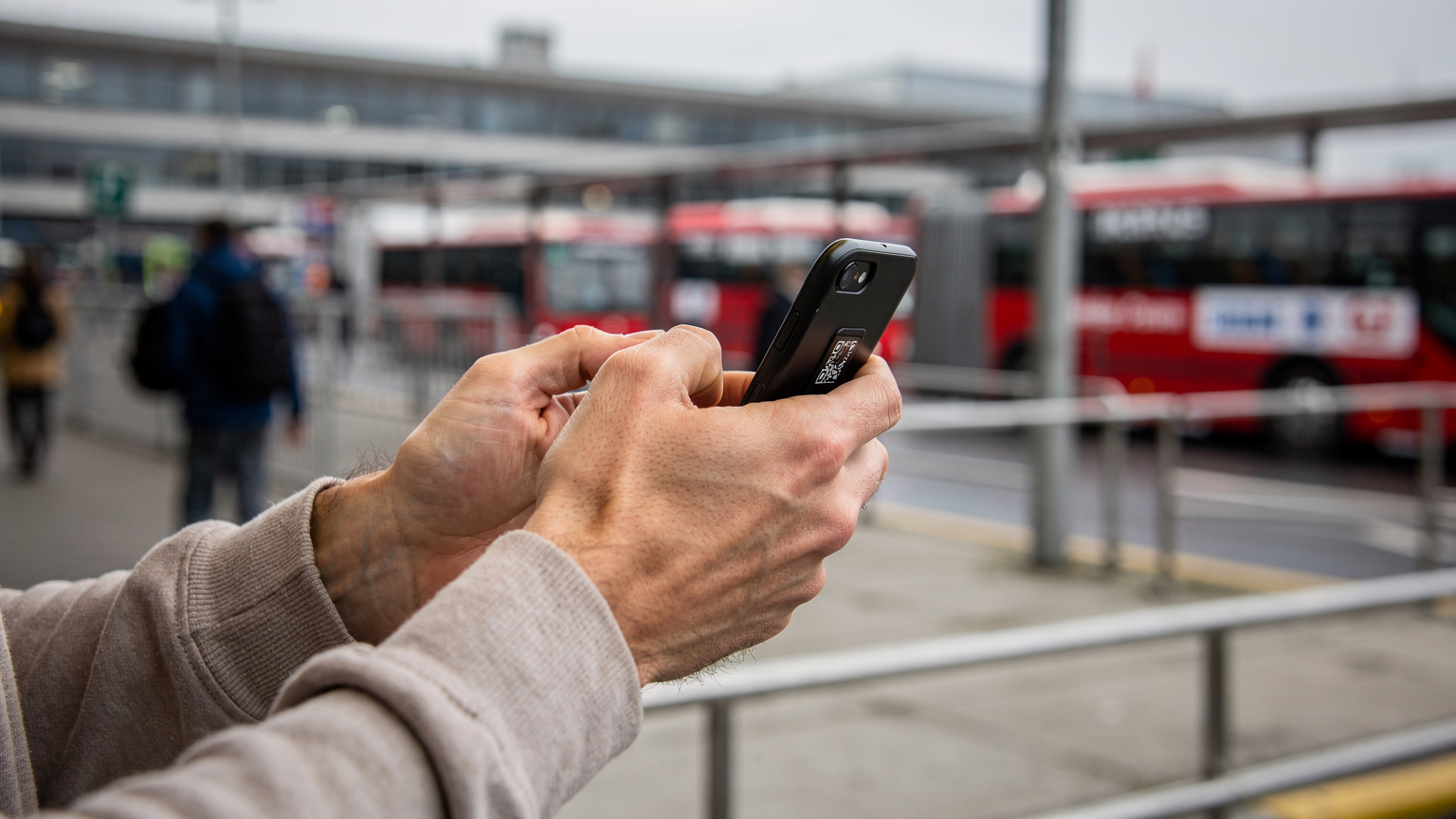 Nahaufnahme eines Smartphones in den Händen eines Reisenden, der gerade einen QR-Code scannt, um eine eSIM zu aktivieren, im Hintergrund verschwimmt eine belebte Busbahnhof-Szene in Belgrad.