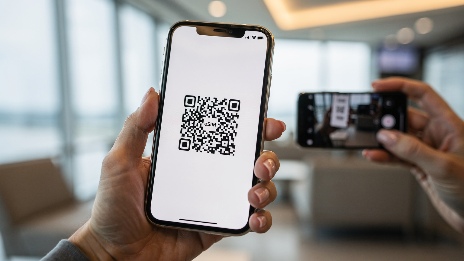 A close-up of a hand holding a smartphone, scanning a QR code for eSIM activation against a blurry backdrop of a modern airport lounge.