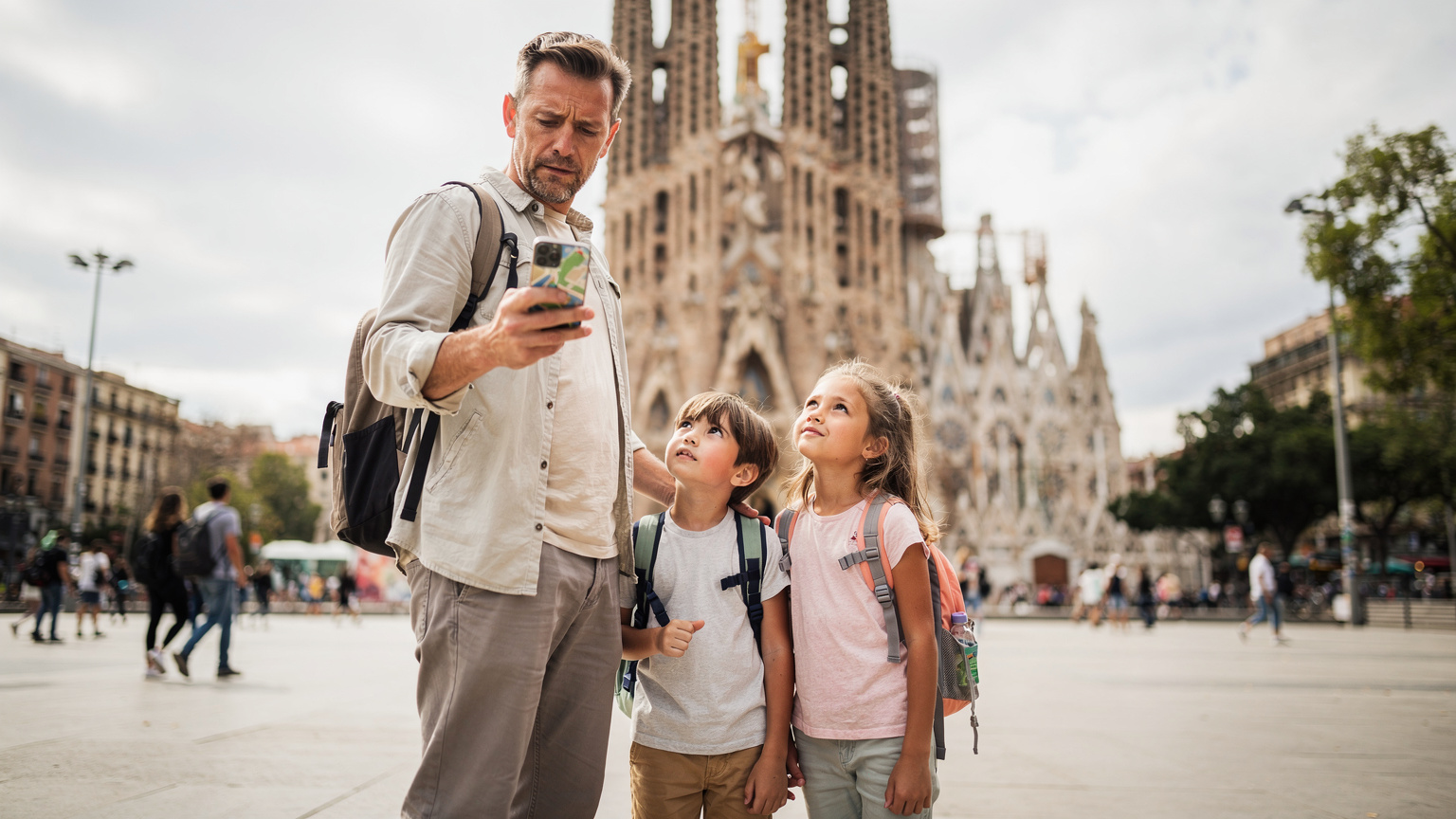 Barcelona'daki Sagrada Familia önünde, elinde akıllı telefonuyla yol tarifi bakan bir baba, iki küçük çocuğu ise çevreyi merakla inceliyor. Telefon ekranında harita uygulaması kısmen görünüyor.