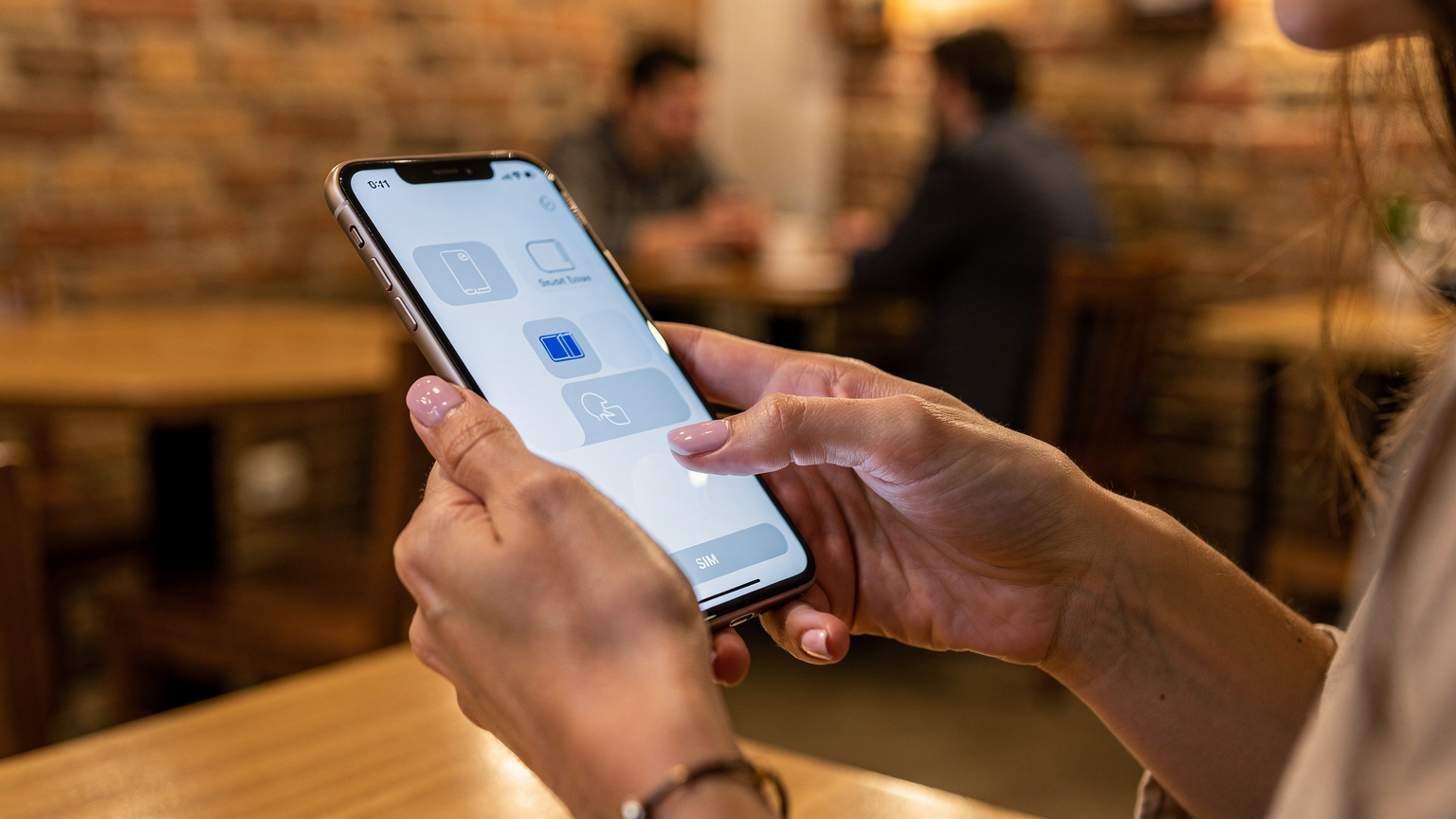 Крупный план женских рук, настраивающих параметры eSIM на современном смартфоне, на заднем плане виднеется размытый интерьер уютного тбилисского кафе с деревянной мебелью и приглушенным освещением.