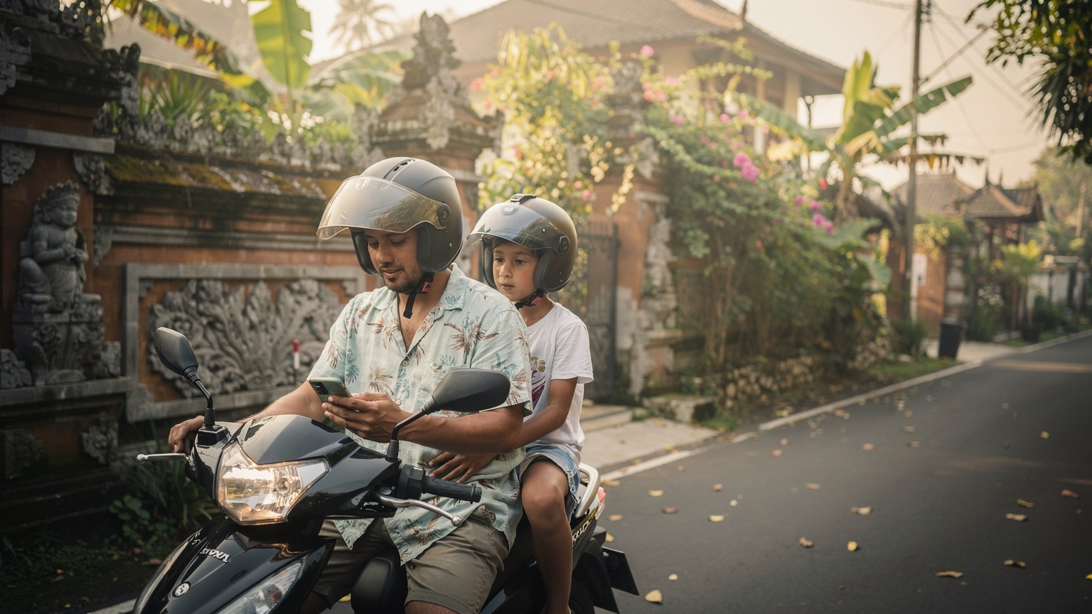A parent checks their phone for directions while sitting on a scooter in a quiet, leafy street in Seminyak, Bali, with a child in a helmet seated behind them. Traditional Balinese wall carvings line the street.