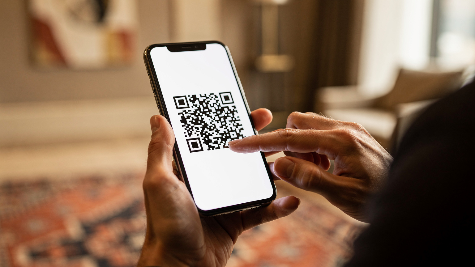 A close-up shot of a pair of human hands holding a modern smartphone, with one hand gently tapping the screen while the other holds it steady, scanning a QR code for eSIM activation. The background is a softly blurred, warm-toned hotel lobby in Ankara, suggesting ease of setup upon arrival.