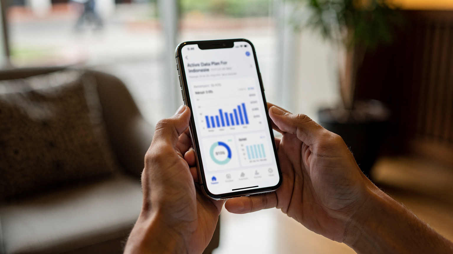 En reisende holder en smarttelefon med Cellesim-appen åpen, viser en dataplan for Indonesia. Bakgrunnen er sløret, men antyder en hotellobby eller et rolig kaféhjørne i Jakarta.