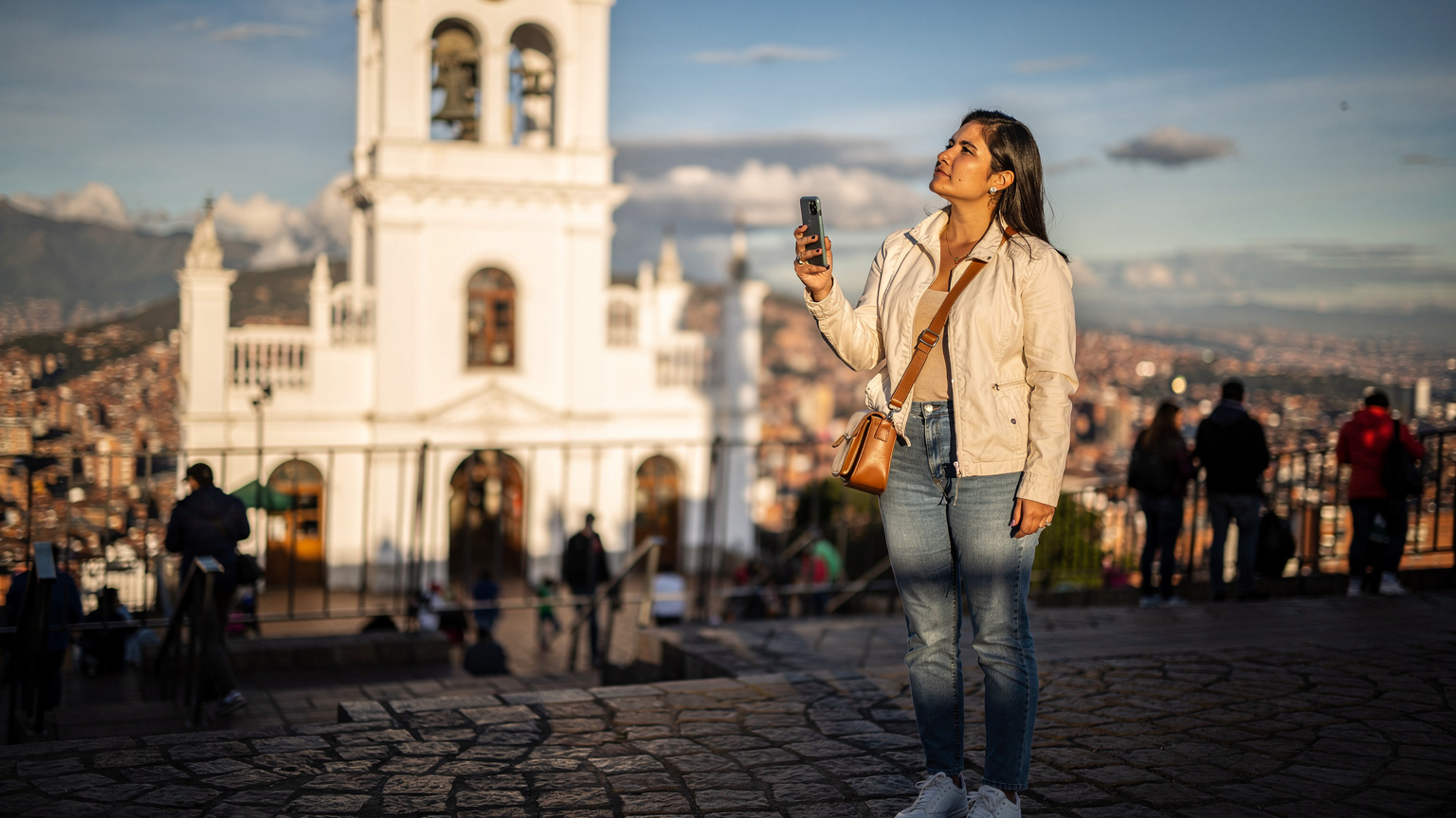 Woman with smartphone at Monserrate Sanctuary, Bogotá, contemplating eSIM options for travel.