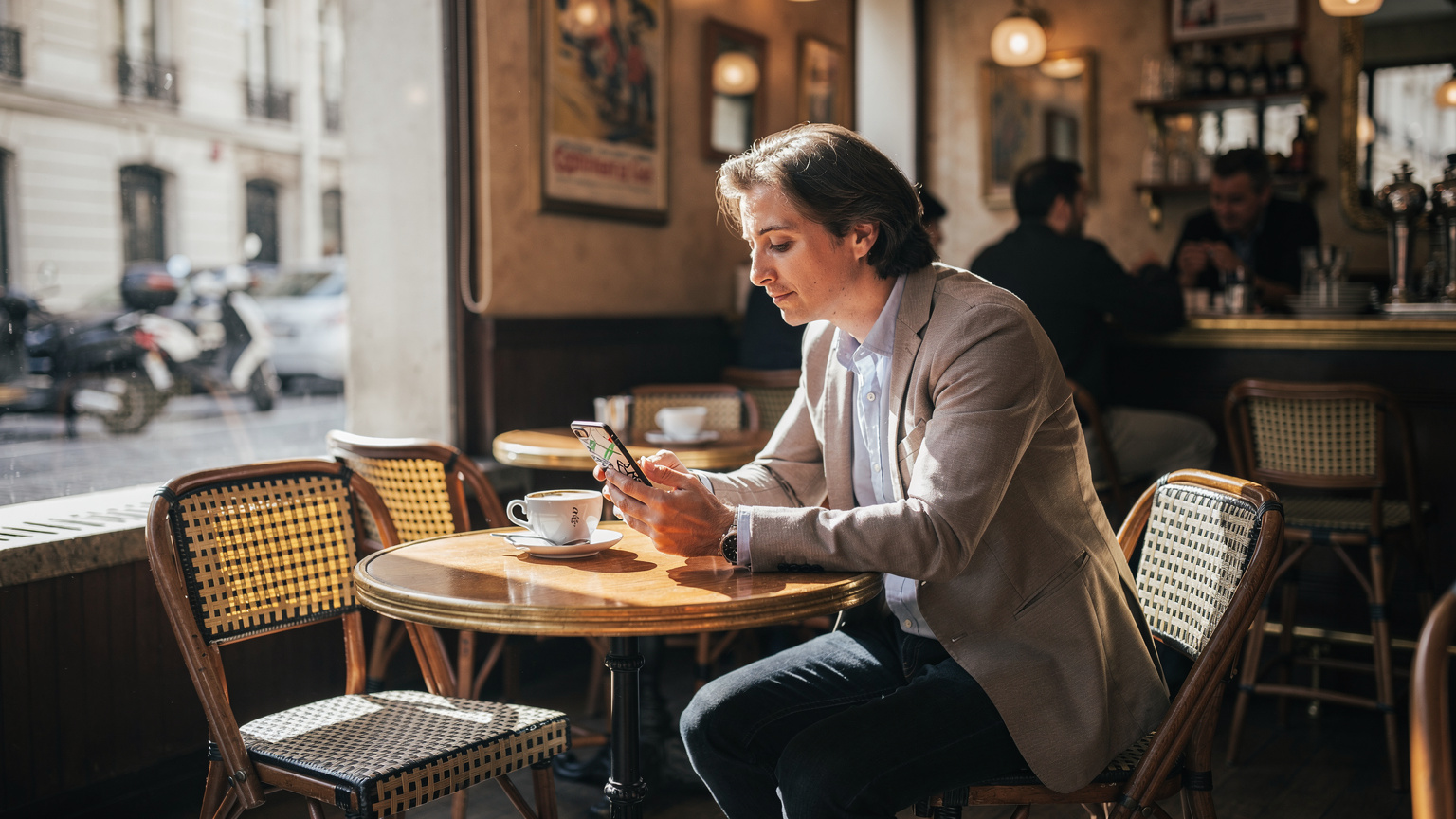 Eine Person sitzt in einem belebten Café in Paris und betrachtet ihr Smartphone, das eine Karte mit einer geplanten Route anzeigt.