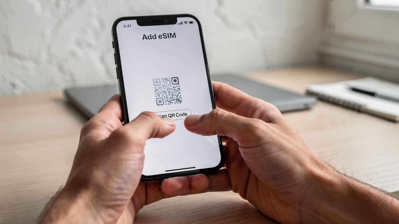 Close-up of human hands holding a smartphone, with the 'Add eSIM' menu visible on the screen, ready to scan a QR code.