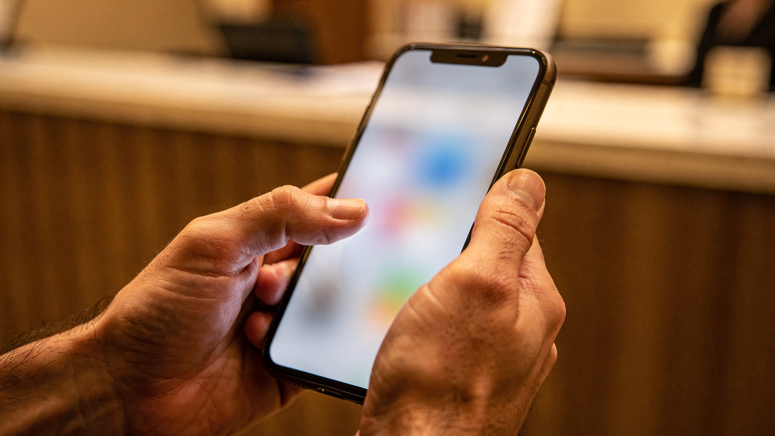 Manos de un viajero deslizan el dedo sobre la pantalla de un smartphone para aceptar una notificación, con un fondo desenfocado de un mostrador de hotel.
