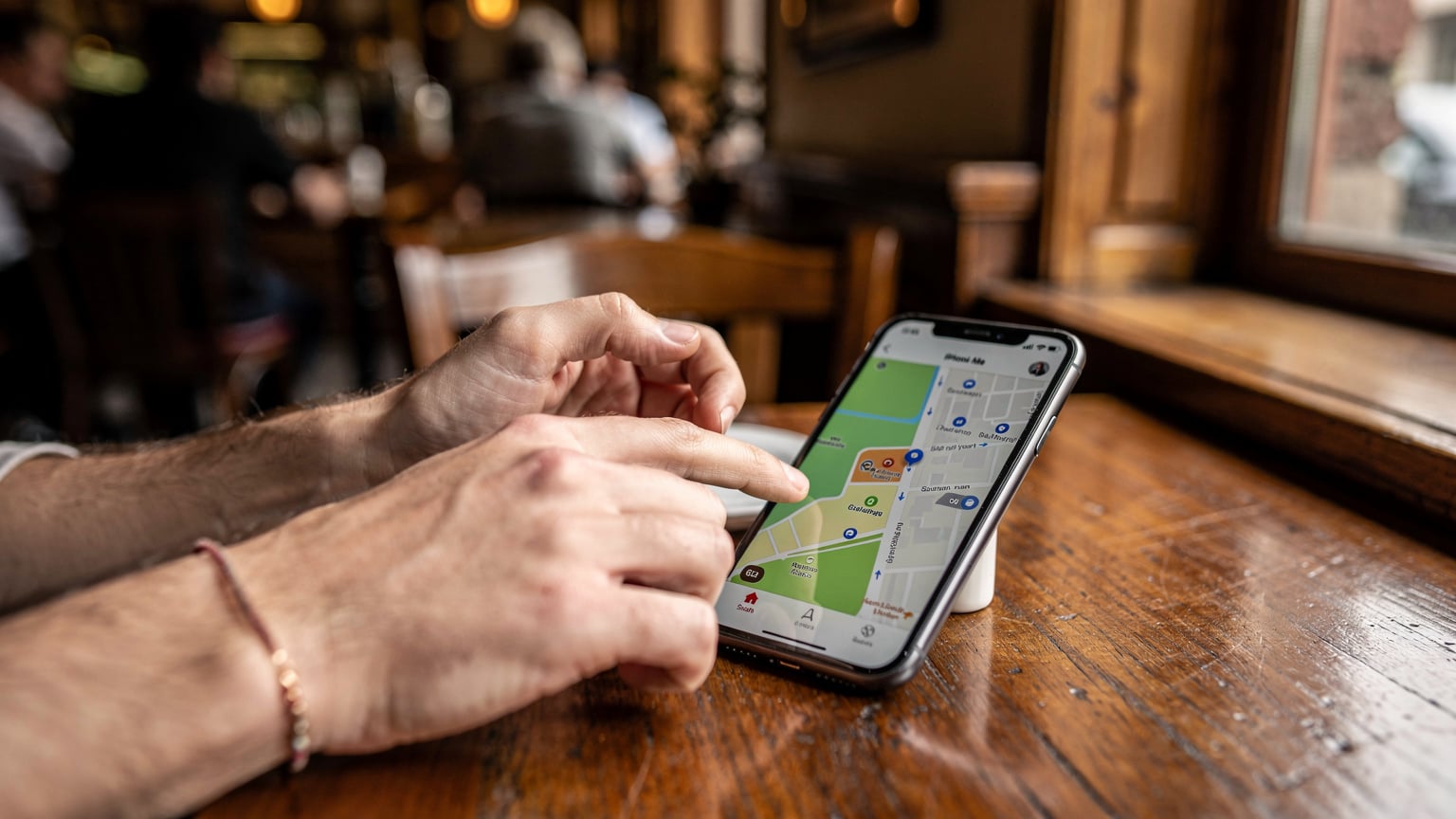 Nahaufnahme der Hände einer Person, die auf einem Smartphone-Bildschirm eine Karte aufruft, während sie an einem Tisch in einem belebten Café in Istanbul sitzt.