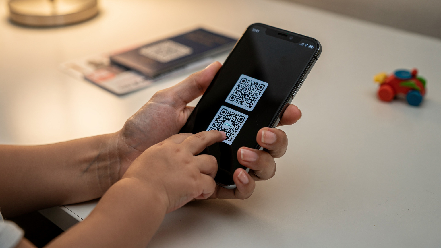 A close-up of a parent's hands setting up an eSIM on a smartphone, with a child's hand gently touching the screen in curiosity.