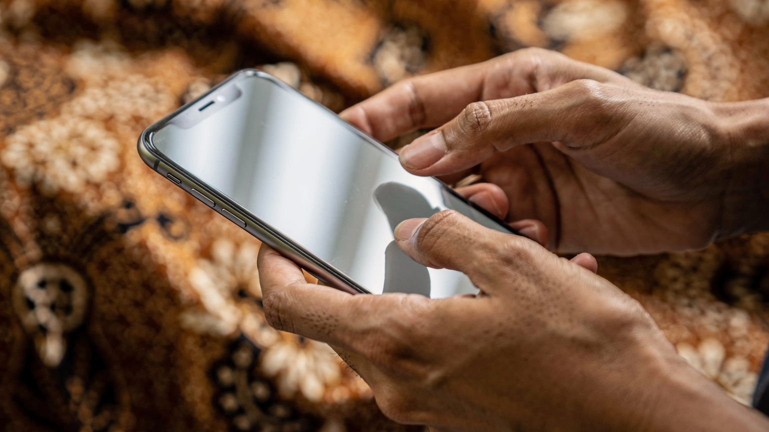 A close-up shot of hands navigating a phone screen, showing the process of entering a QR code for eSIM activation, with a blurred Indonesian batik pattern in the background.