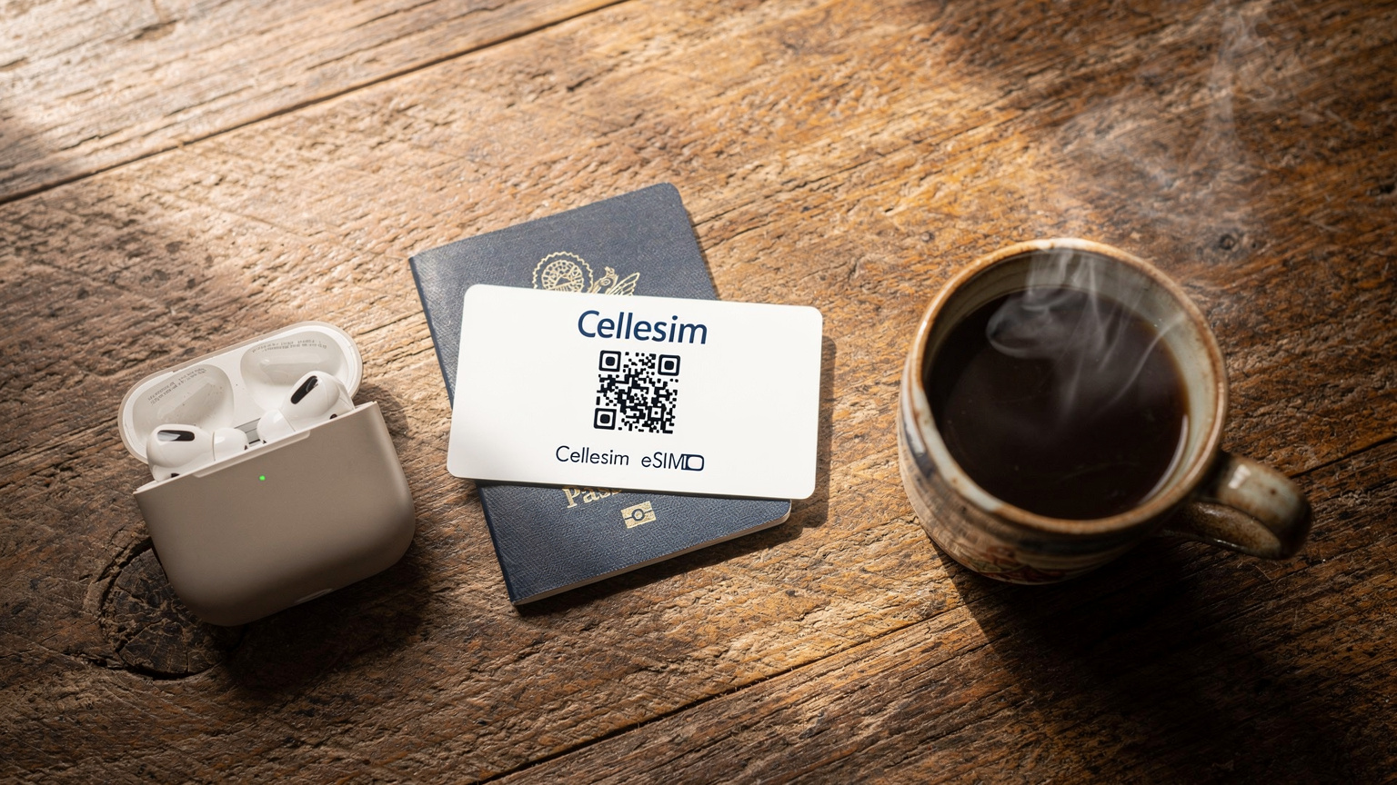 An editorial overhead flat-lay shot on a rustic wooden table, featuring a passport, a Cellesim eSIM QR code printout, a pair of wireless earbuds, and a small, locally-crafted Balinese coffee cup, emphasizing pre-travel preparation.