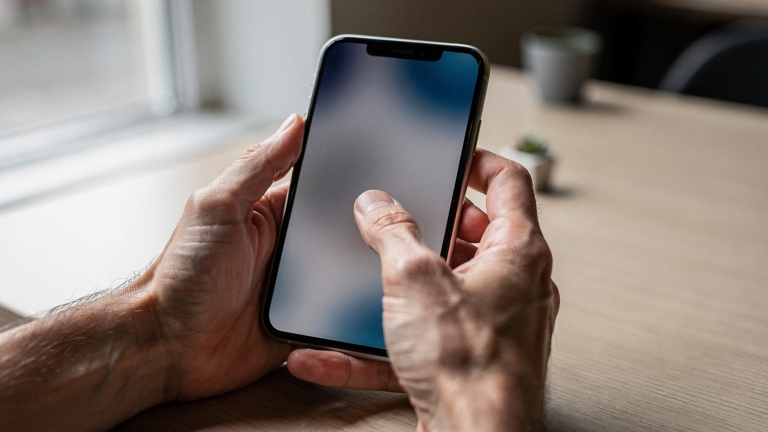 Nahaufnahme von Händen, die ein iPhone 11 halten, während der Daumen über den Bildschirm streicht, um eine Einstellung zu ändern. Keine Texte oder Symbole auf dem Bildschirm sichtbar.