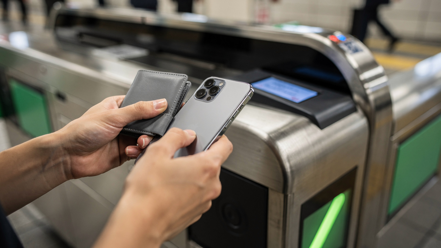 A close-up of human hands, one holding a smartphone to a train station ticket barrier for scanning, in the modern Shibuya Station in Tokyo, Japan.