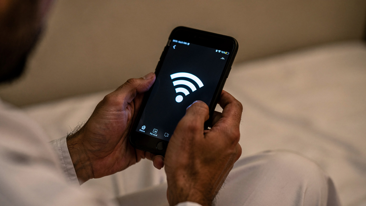 Tangan jemaah haji memegang telefon dengan ikon Wi-Fi lemah dalam bilik hotel.