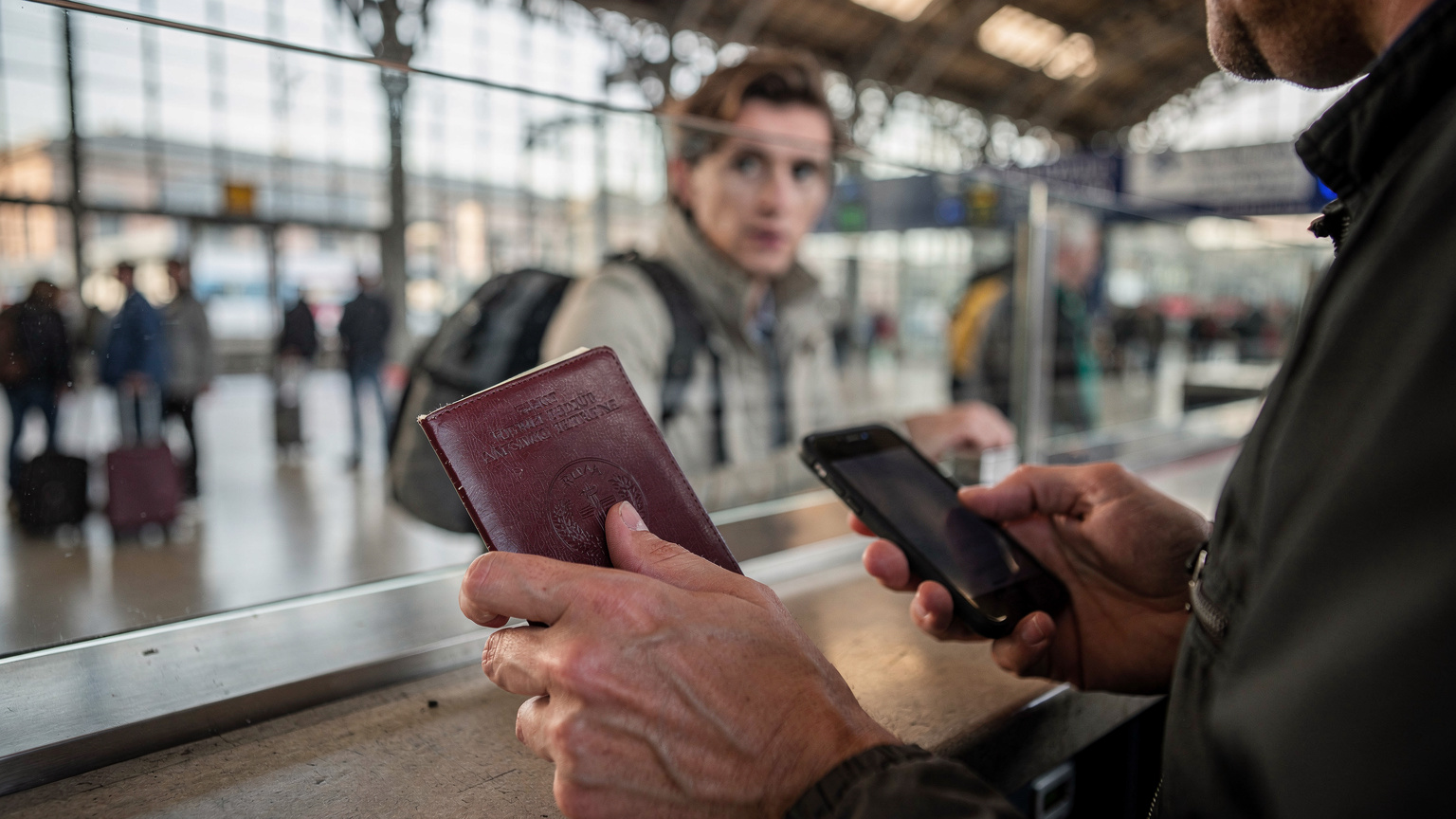 Roma Termini İstasyonu'nda bir tren bileti gişesinde, pasaportunu ve telefonunu tutan bir gezginin yakın çekimi. Yüzündeki hafif bir endişe okunuyor.