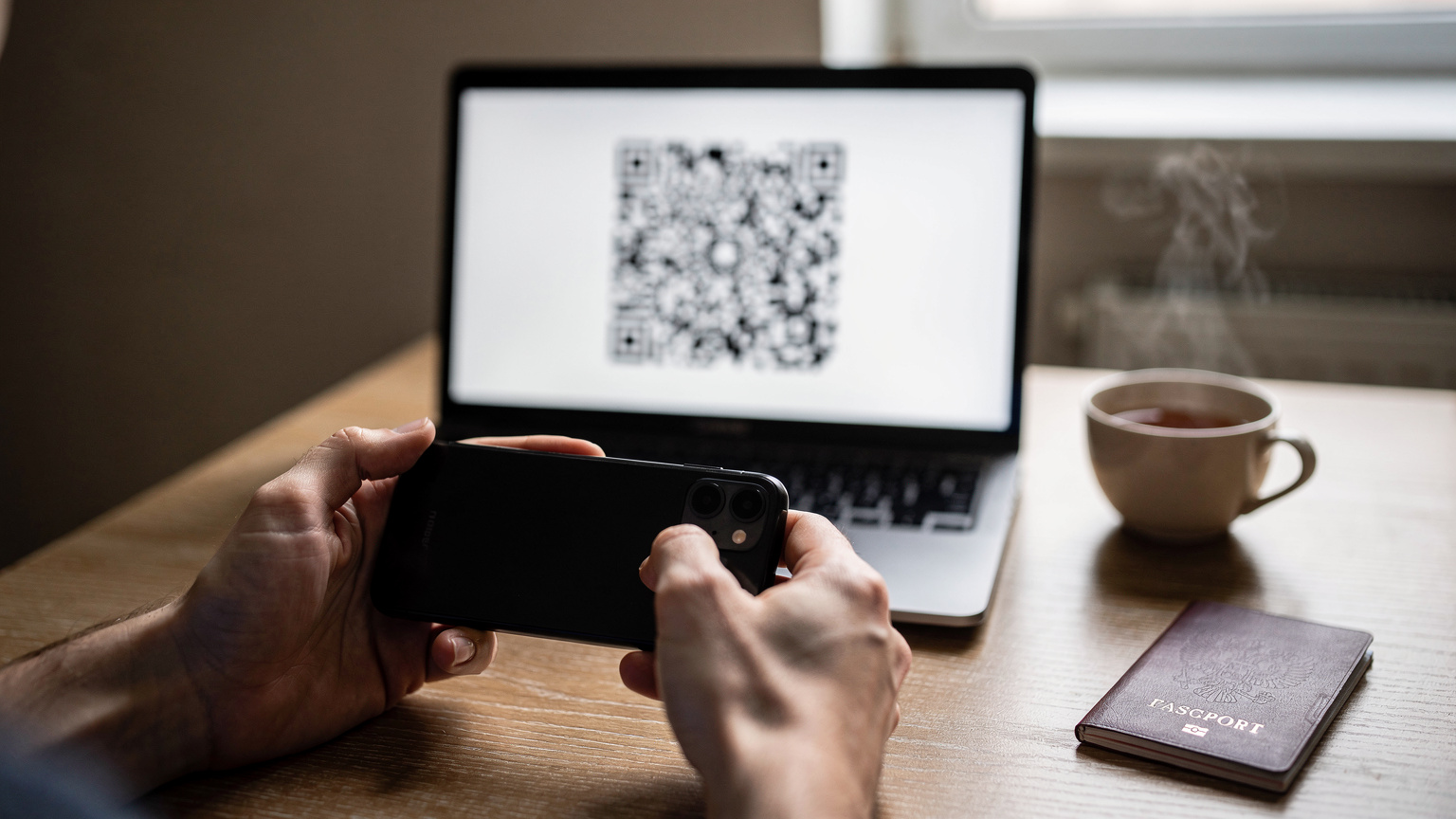 Крупный план рук, сканирующих QR-код на экране ноутбука камерой смартфона