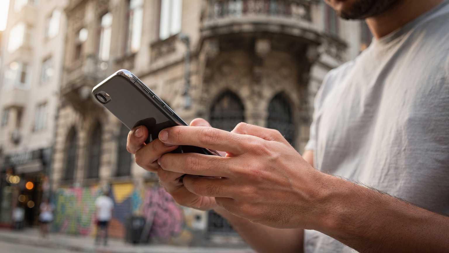 İstanbul'daki tarihi bir telekomünikasyon binasının önünde, sabah güneşinin vurduğu, elinde akıllı telefon tutan bir kişinin yakından çekilmiş görüntüsü.