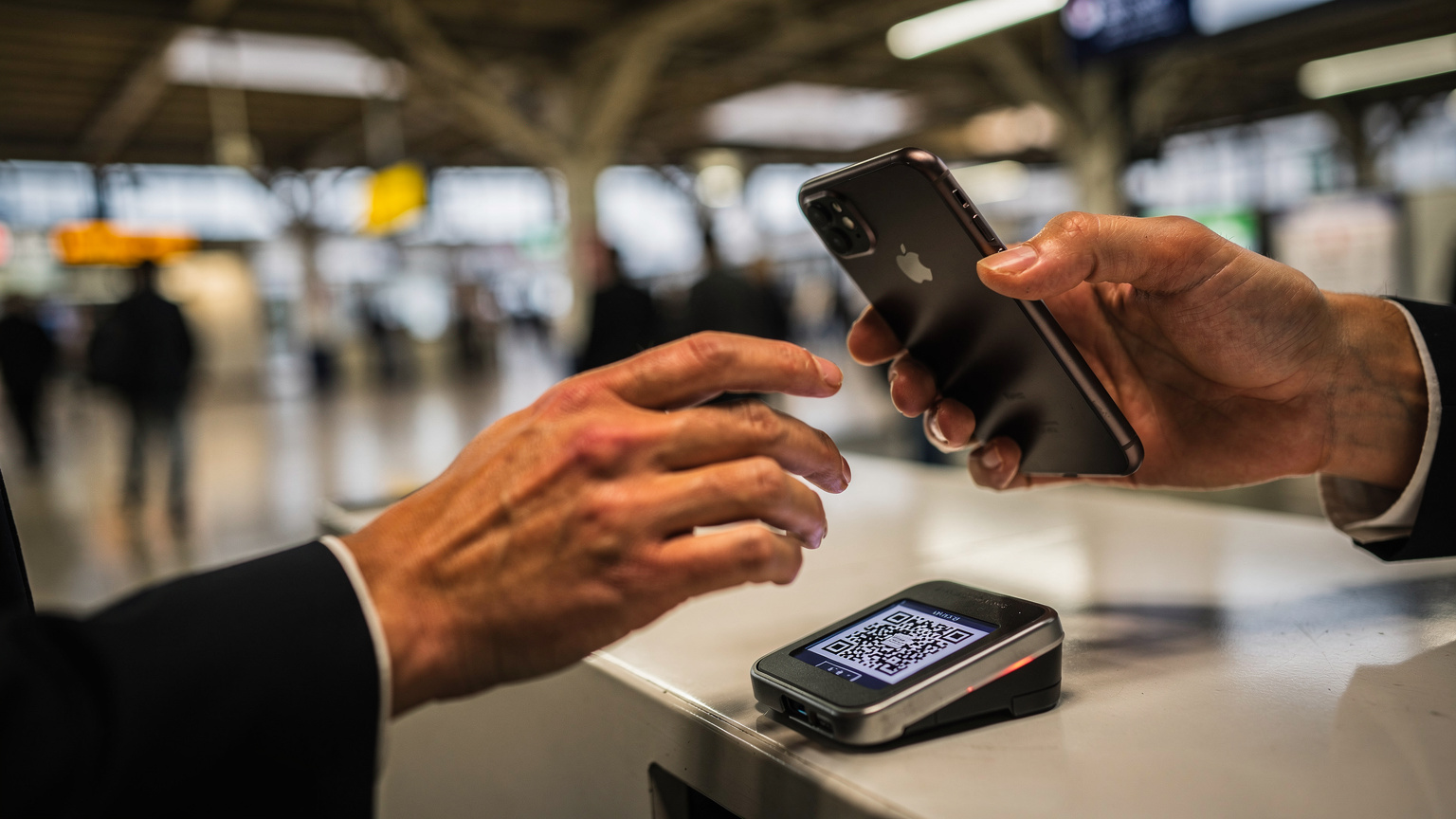Primer plano de las manos de un viajero escaneando un código QR en el mostrador de la estación de Shinjuku, con pantalla girada para que no se vea la interfaz.