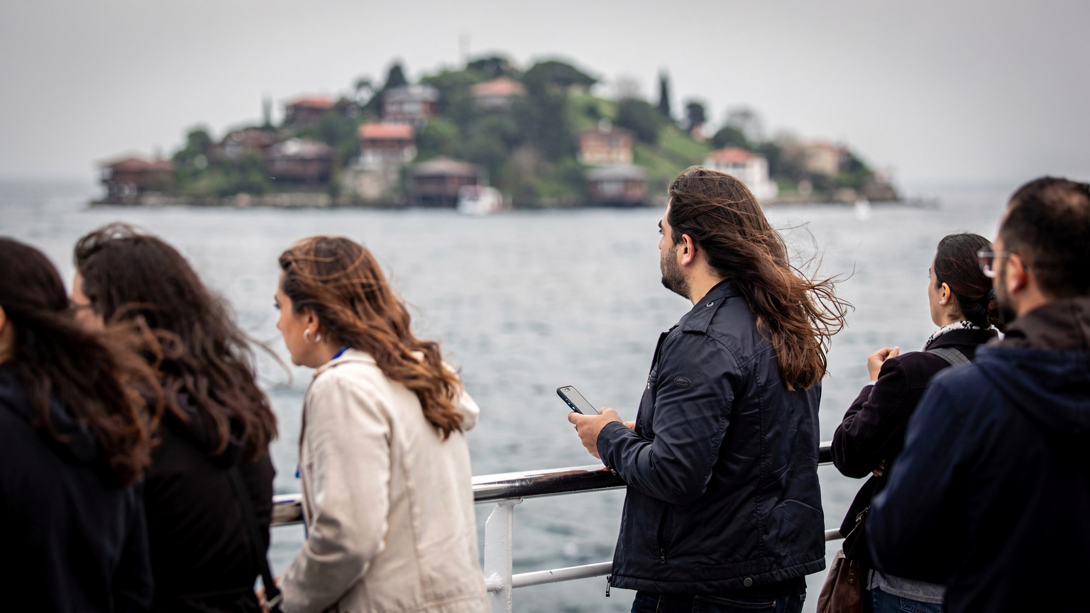 Passeggeri sul ponte del traghetto in avvicinamento a Büyükada, telefono in mano senza guardarlo