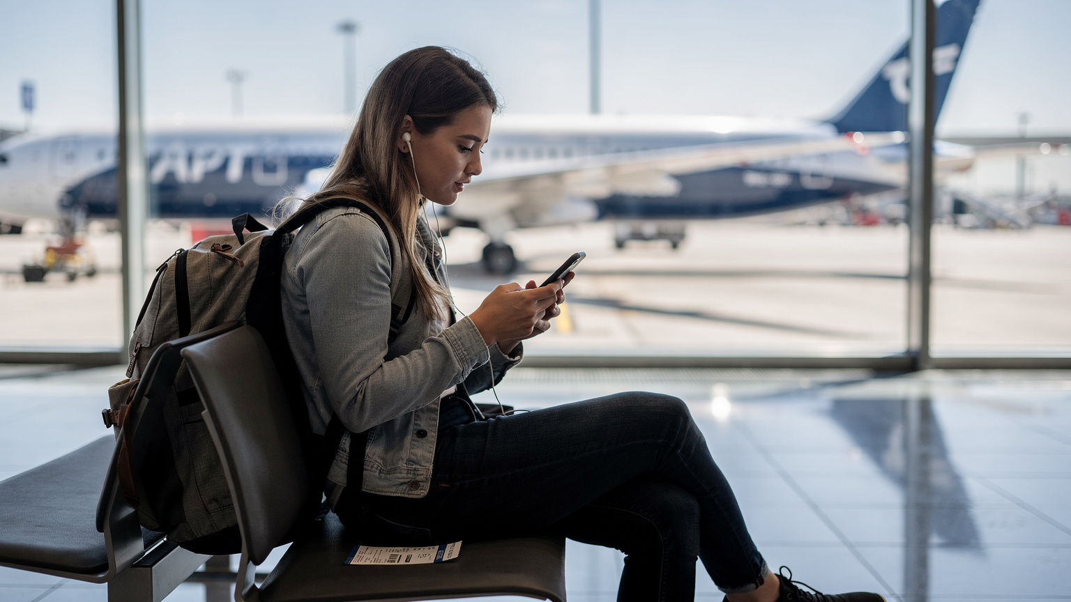 Woman watching Netflix on phone at Copenhagen Airport gate, Boeing 787 visible outside.