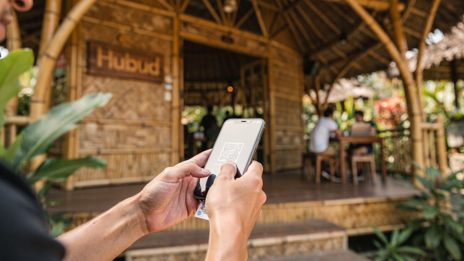 Bali'deki Hubud co-working space'in girişinde, elindeki telefonla bir QR kodu tarayan bir gezginin yakın çekimi.
