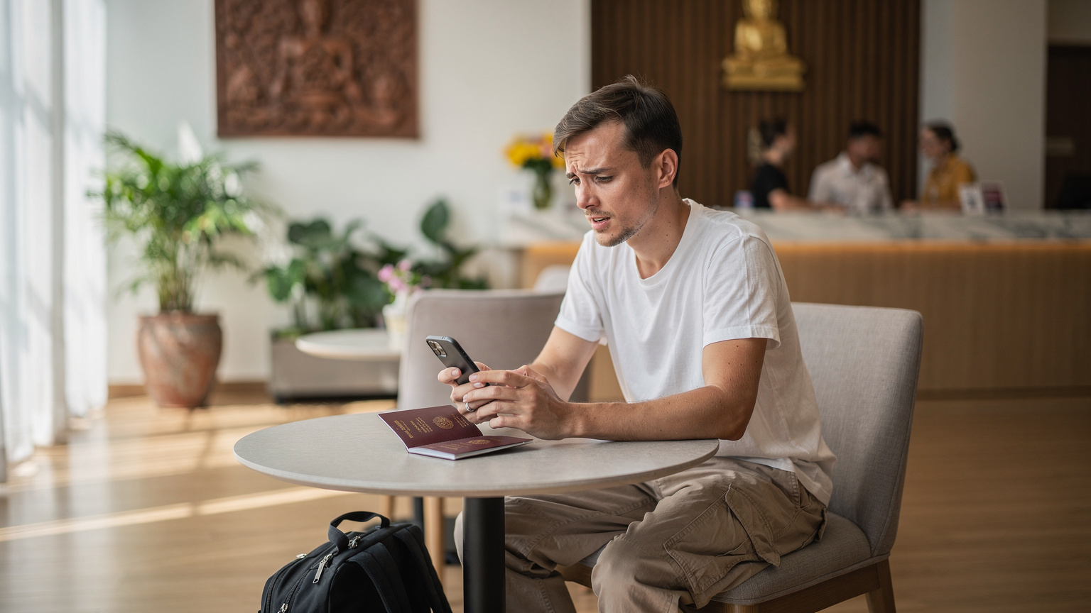 Tayland'daki bir otelin lobi alanında, pasaportunu ve telefonunu masaya koymuş, eSIM bağlantı sorunuyla uğraşan bir gezginin endişeli ifadesi.