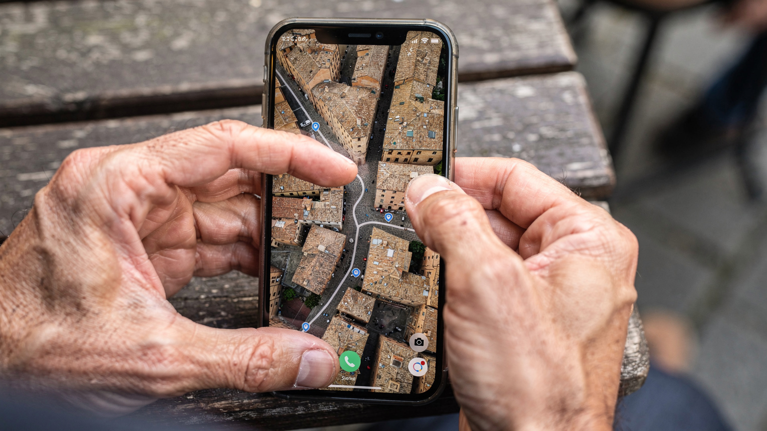 Eine Nahaufnahme menschlicher Hände, die ein Smartphone halten. Auf dem Bildschirm ist eine detaillierte Offline-Karte von Maps.me mit einer markierten Route in einer unbekannten Stadt zu sehen. Die Hände deuten auf einen Punkt auf dem Bildschirm, der eine Navigation anzeigt.