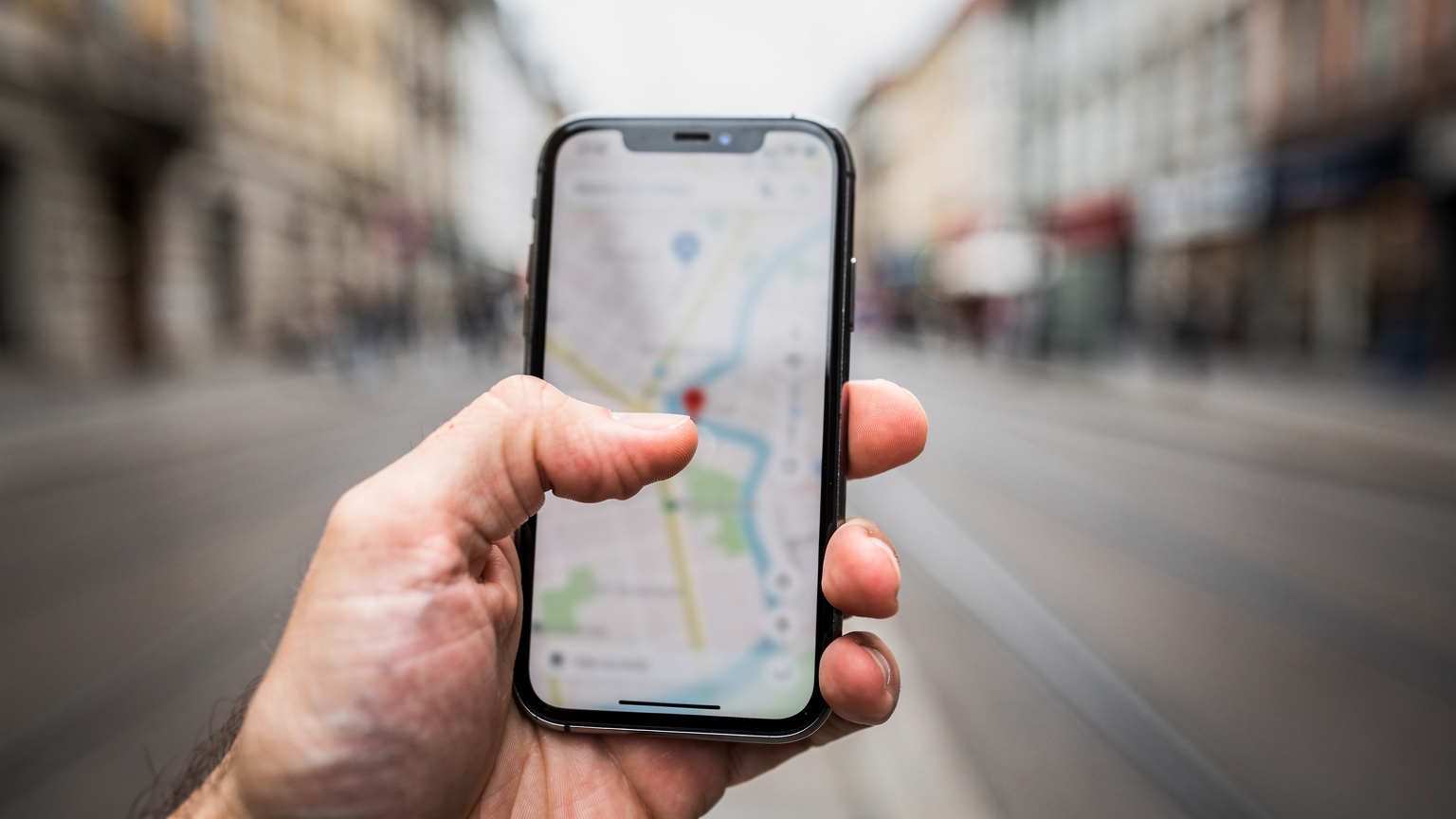 A close-up of a traveler's hand hovering over a digital map on a smartphone screen, looking slightly concerned, with the blurred background suggesting a busy street in a foreign city, perhaps near a tram line.