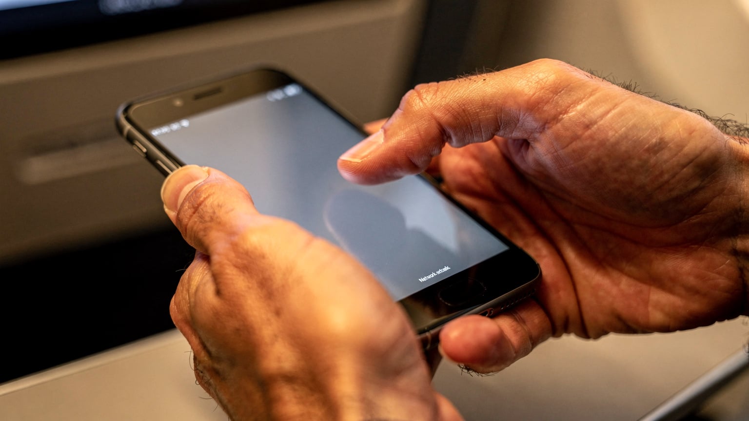 Close-up of human hands holding a smartphone, with fingers tapping on a settings menu, about to activate a new eSIM profile.