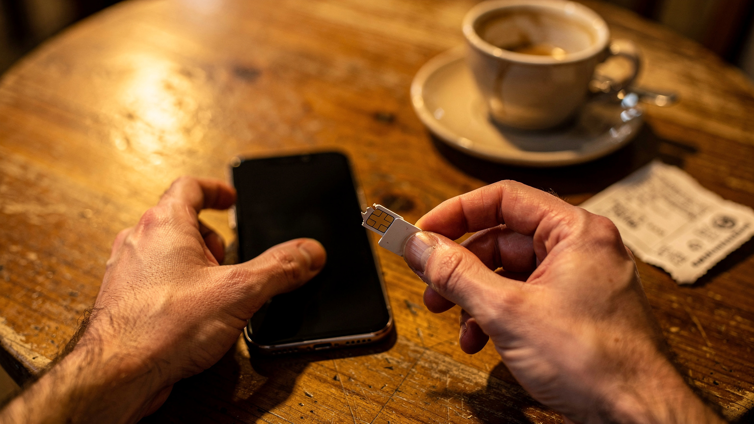 Mãos de um viajante a segurar um smartphone e um cartão SIM físico partido ao meio
