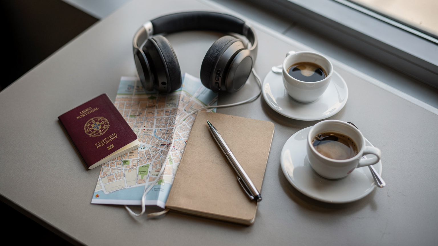 Vista aérea de uma mesa de aeroporto com passaporte, fones de ouvido e um mapa dobrado