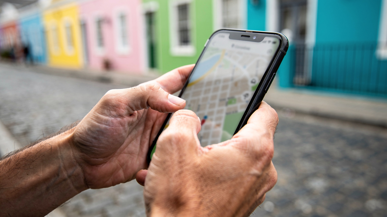 Ruce turisty navigují mapu na chytrém telefonu v Kapském Městě, s rozmazanými historickými budovami v pozadí.