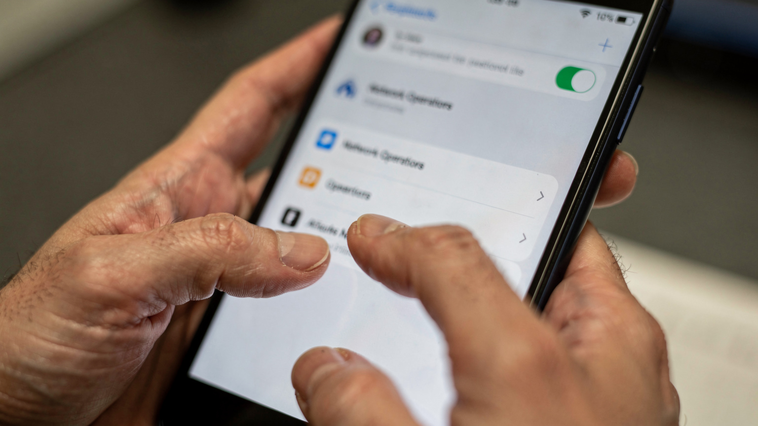 A close-up of a person's hands as they manually select a network operator from a list on a phone screen, with the surrounding interface blurred.