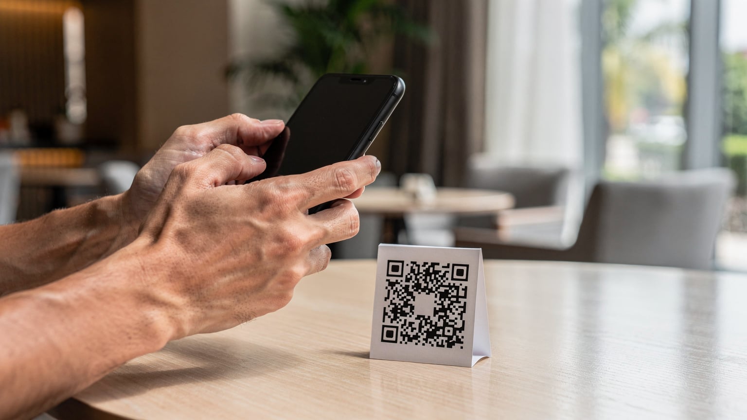 A traveler uses their phone to scan a QR code at a desk in a modern hotel lobby in Jakarta, with their passport and a cup of coffee nearby.