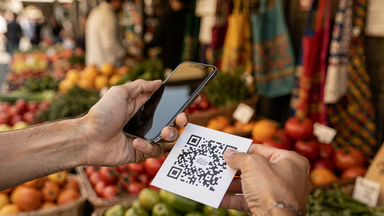 A parent's hands holding a smartphone, scanning a QR code on a piece of paper, with a blurry Italian market stall in the background.