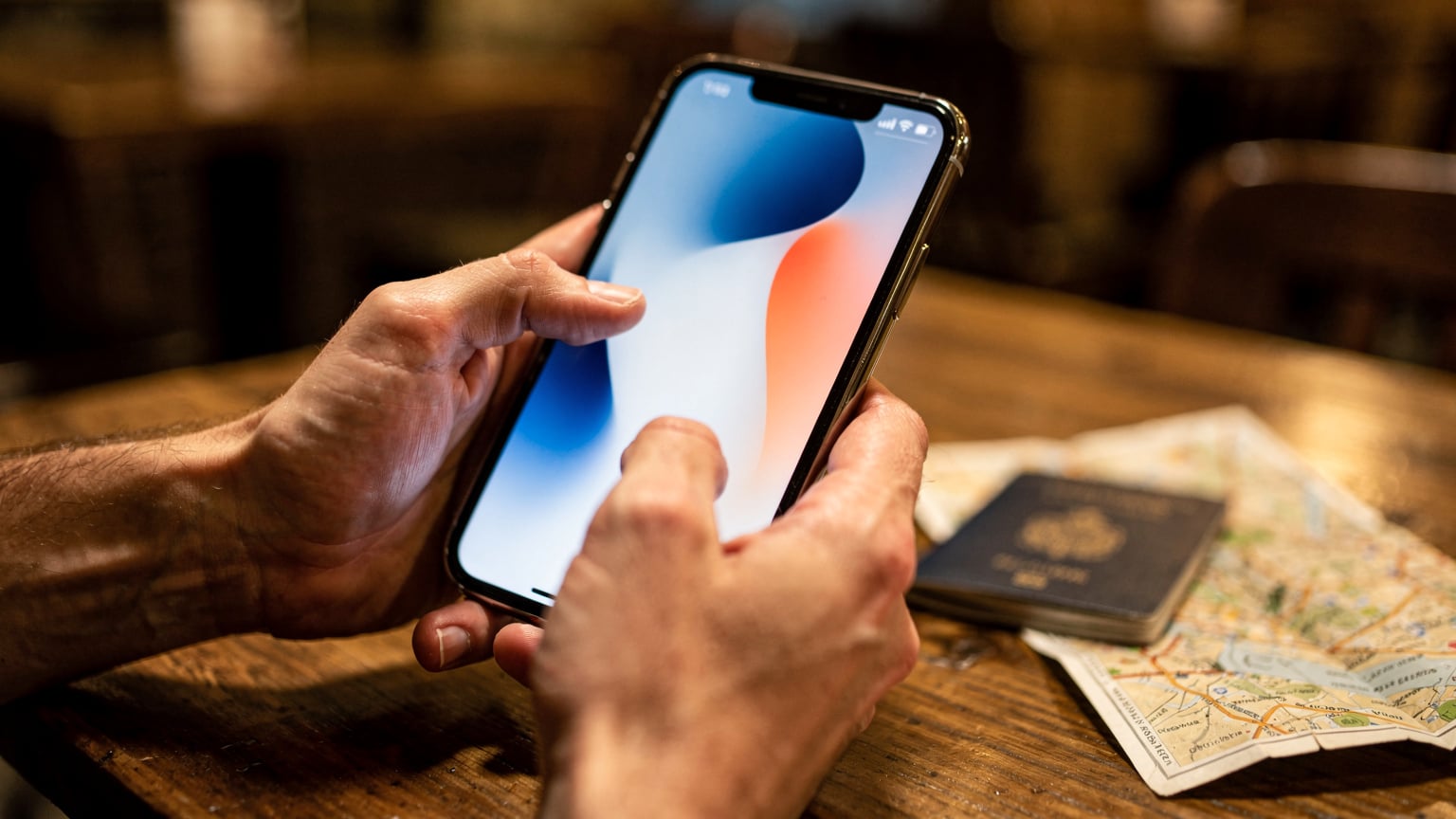 Nahaufnahme von Händen, die ein Smartphone halten, wobei der Fokus auf den Daumen liegt, der über den Bildschirm wischt. Im Hintergrund verschwimmen Reiseunterlagen wie ein Reisepass und eine gedruckte Karte auf einem Tisch in einem Café in Belgrad.