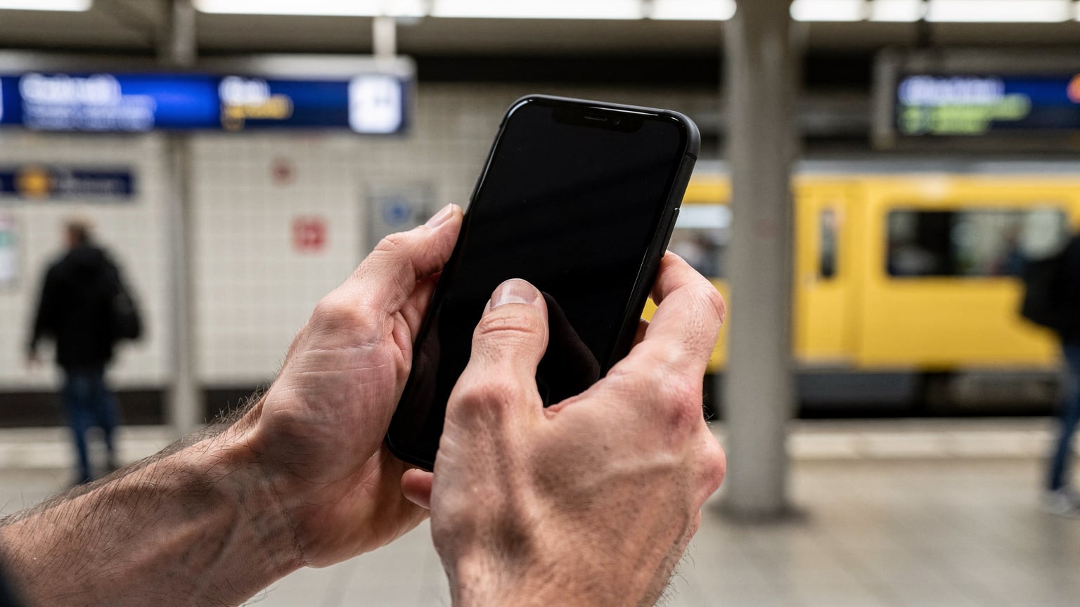 A close-up of hands swiping on a smartphone screen inside a train station in Berlin.