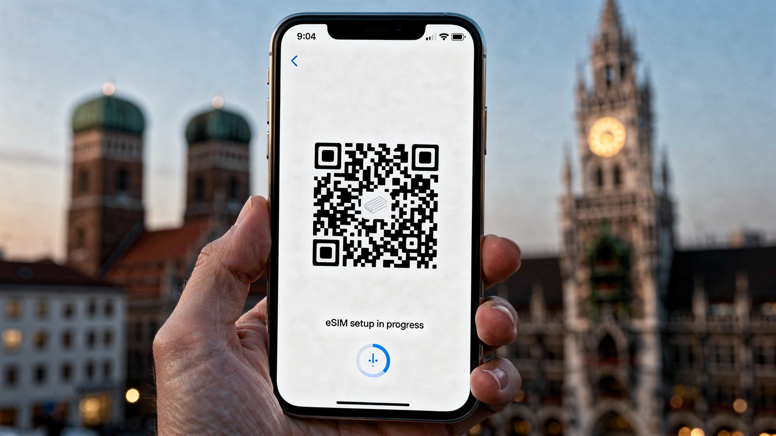 Bir akıllı telefon ekranında eSIM kurulumu için QR kod tarama işlemi gösteriliyor, arka planda Münih'in simgesel yapıları bulanık bir şekilde görünüyor.