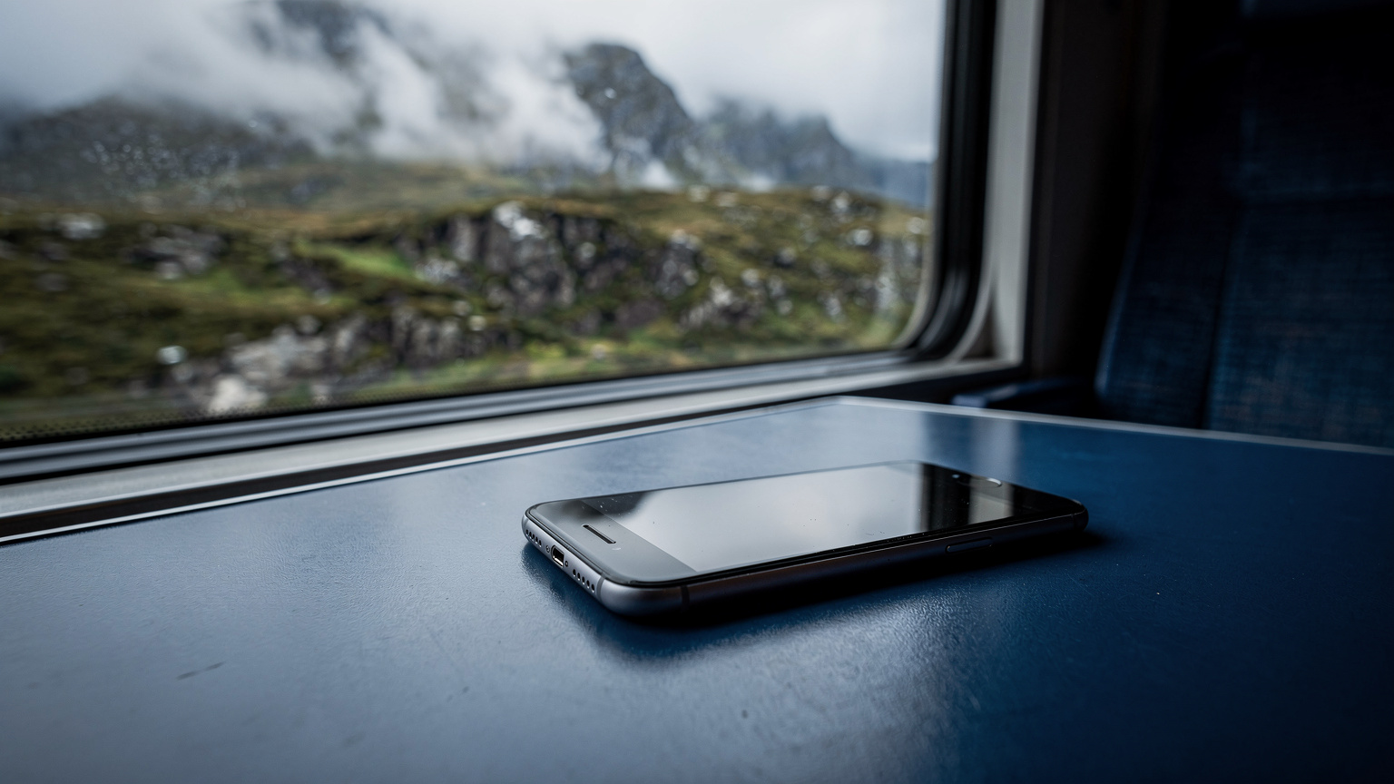 A smartphone resting on a train table next to a window showing a blurry Scottish landscape.
