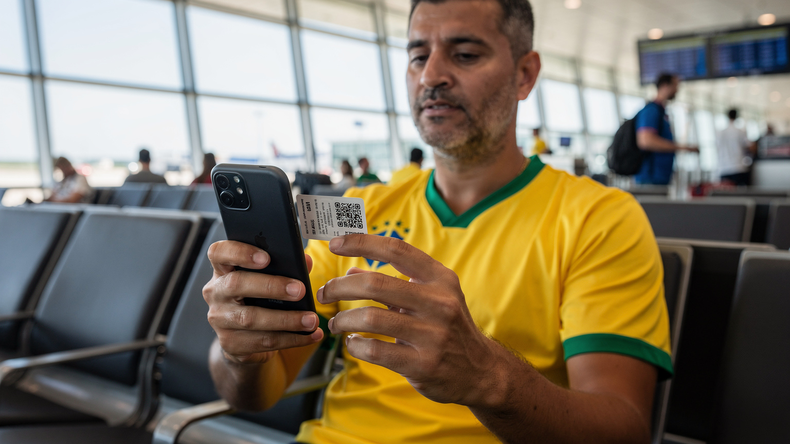 Um torcedor brasileiro, vestindo a camisa da seleção, usando o celular para escanear um QR code de ativação de eSIM no saguão de um aeroporto movimentado, com sua bagagem de mão ao lado.
